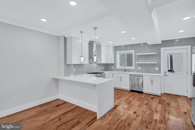 kitchen with a peninsula, a sink, stainless steel appliances, white cabinetry, and wall chimney exhaust hood