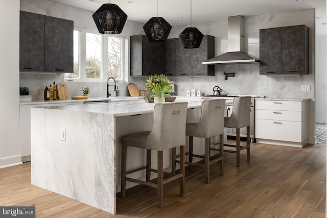 kitchen featuring tasteful backsplash, a center island, light wood-style floors, wall chimney range hood, and stove