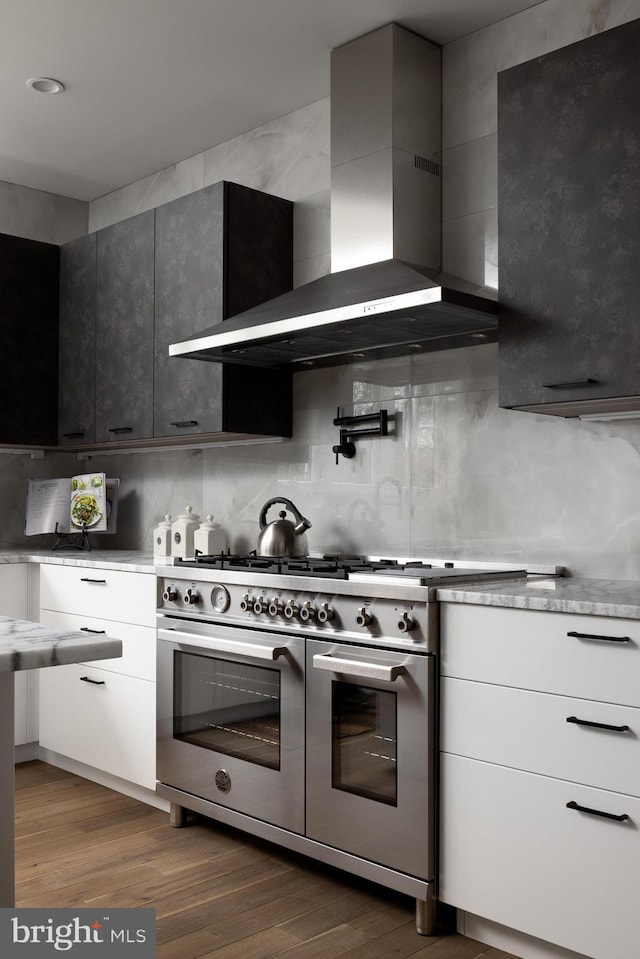 kitchen with decorative backsplash, range with two ovens, wall chimney exhaust hood, and dark wood-style flooring