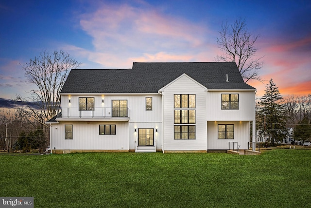 back of house with a balcony, a lawn, and a shingled roof