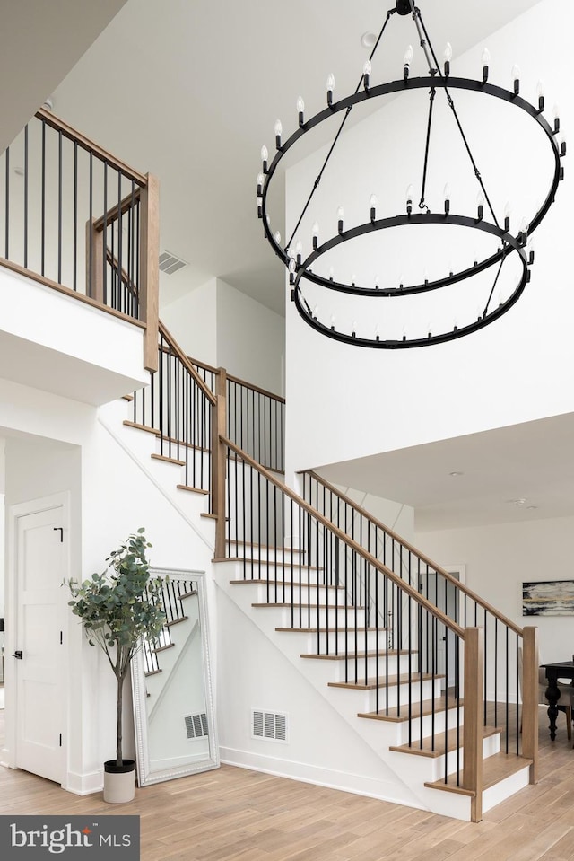 staircase with visible vents, baseboards, wood finished floors, and a towering ceiling