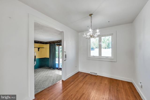 unfurnished dining area featuring baseboards, visible vents, an inviting chandelier, wood-type flooring, and a textured ceiling