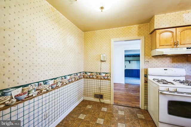 kitchen featuring visible vents, wallpapered walls, gas range gas stove, under cabinet range hood, and stone finish flooring