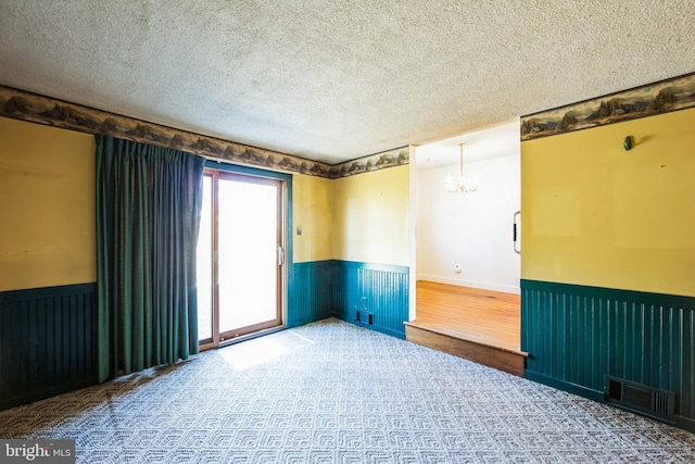 unfurnished room with a wainscoted wall, visible vents, a chandelier, and a textured ceiling