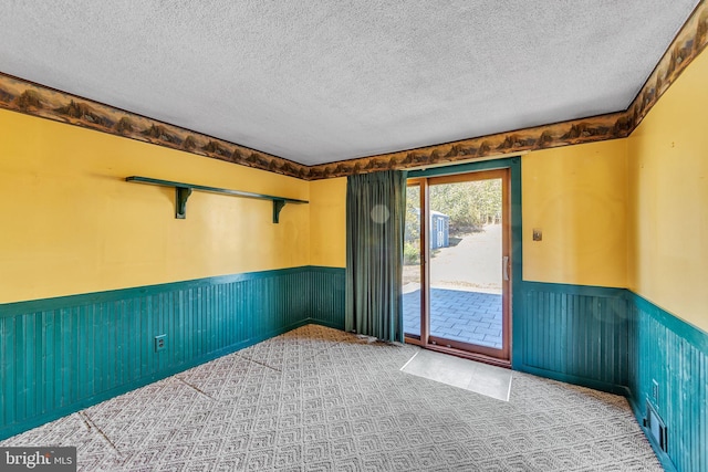 carpeted spare room with a textured ceiling and wainscoting