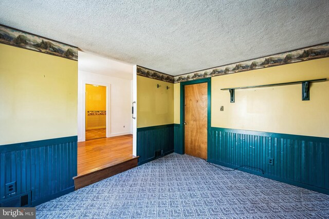 empty room featuring visible vents, a textured ceiling, and wainscoting