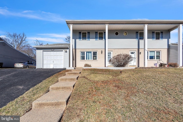 view of front of property with aphalt driveway, an attached garage, brick siding, and a front yard