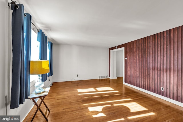 unfurnished room with wooden walls, baseboards, visible vents, and wood finished floors