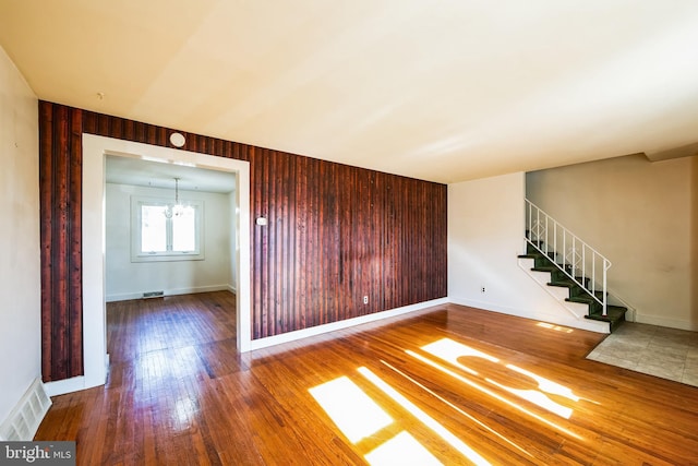 unfurnished room featuring hardwood / wood-style floors, visible vents, an inviting chandelier, stairs, and wood walls