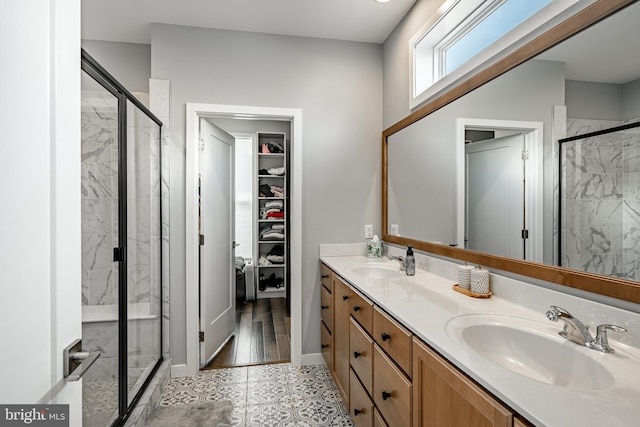 bathroom with double vanity, a marble finish shower, and a sink