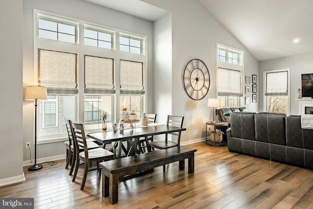 dining space with baseboards, wood-type flooring, and high vaulted ceiling