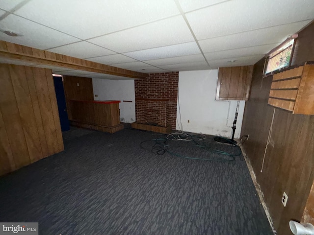 finished below grade area featuring wooden walls, carpet flooring, and a drop ceiling