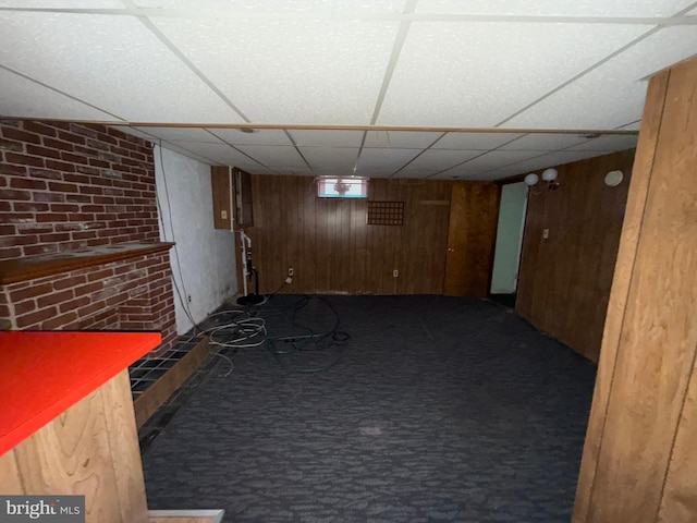 finished below grade area featuring a paneled ceiling, carpet, and wood walls