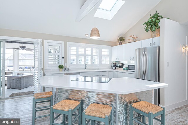 kitchen with a kitchen bar, light countertops, black electric stovetop, and freestanding refrigerator