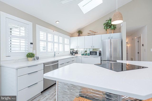 kitchen with pendant lighting, light countertops, a skylight, white cabinets, and stainless steel appliances