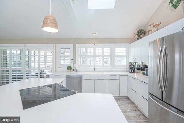 kitchen with a sink, stainless steel appliances, vaulted ceiling with skylight, white cabinets, and light countertops