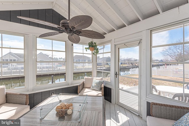 sunroom / solarium featuring a healthy amount of sunlight, lofted ceiling with beams, ceiling fan, and a water view