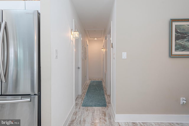 hallway featuring attic access, light wood-type flooring, and baseboards