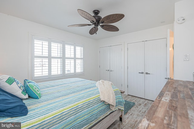 bedroom with light wood finished floors, two closets, and ceiling fan