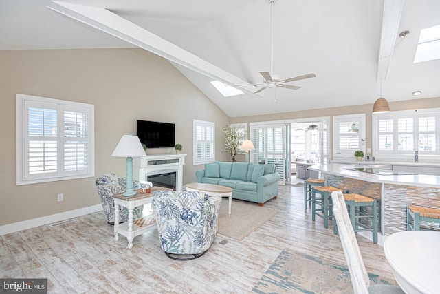 living room featuring a ceiling fan, baseboards, high vaulted ceiling, a skylight, and a high end fireplace