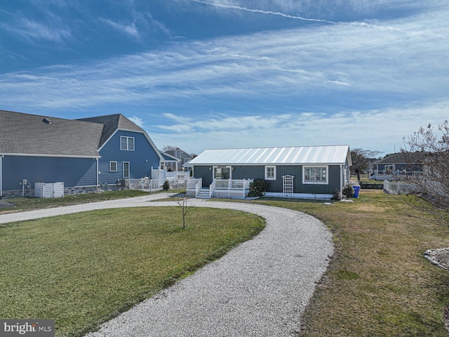 view of front facade with a front lawn, metal roof, fence, and curved driveway