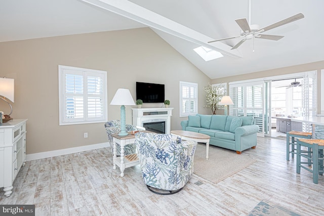 living area with baseboards, a fireplace, ceiling fan, beamed ceiling, and light wood-type flooring