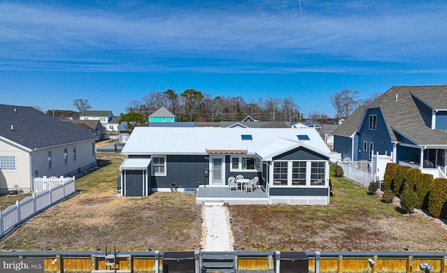 back of property featuring metal roof, a residential view, a fenced backyard, and a sunroom