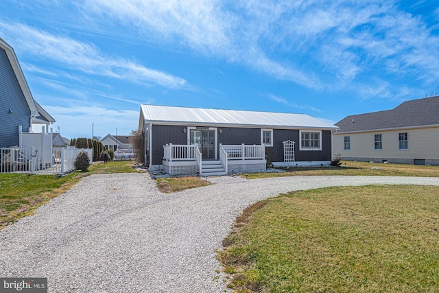 manufactured / mobile home with fence, driveway, covered porch, a front lawn, and metal roof