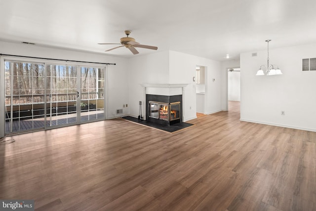 unfurnished living room with a glass covered fireplace, wood finished floors, ceiling fan with notable chandelier, and visible vents