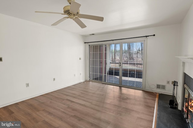 unfurnished living room featuring a glass covered fireplace, wood finished floors, visible vents, and a ceiling fan