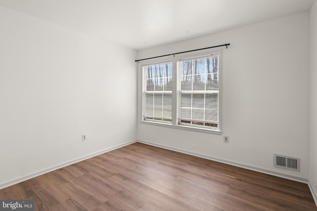 unfurnished room featuring wood finished floors, visible vents, and baseboards