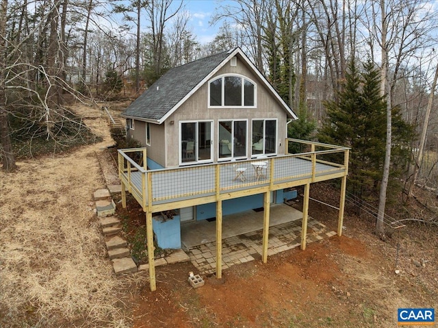 rear view of house featuring a patio, stucco siding, roof with shingles, and a wooden deck