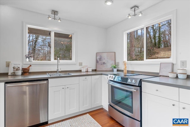 kitchen featuring a sink, stainless steel appliances, white cabinets, dark countertops, and light wood-type flooring