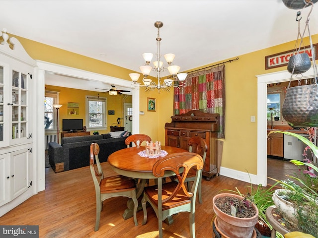 dining space with ceiling fan with notable chandelier, radiator heating unit, wood finished floors, and baseboards