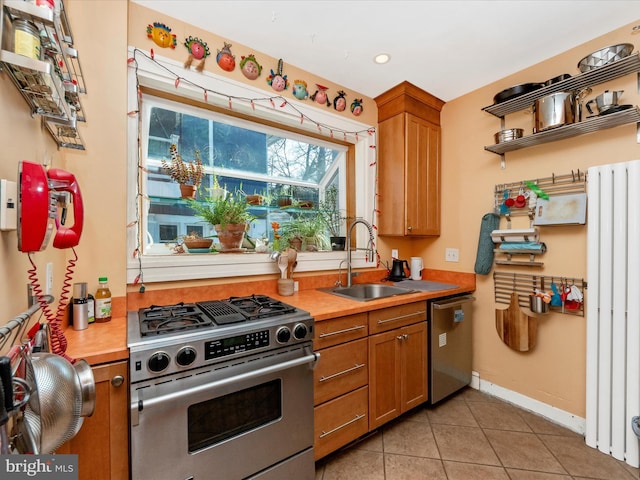 kitchen featuring light tile patterned floors, brown cabinetry, a sink, light countertops, and appliances with stainless steel finishes