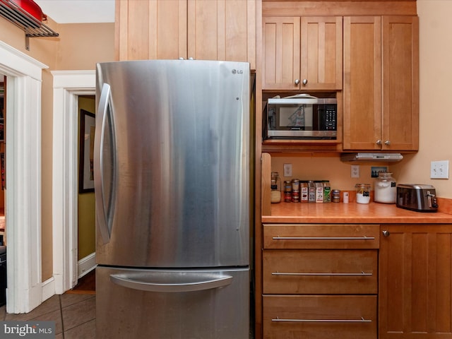 kitchen featuring brown cabinets, dark tile patterned flooring, appliances with stainless steel finishes, and light countertops