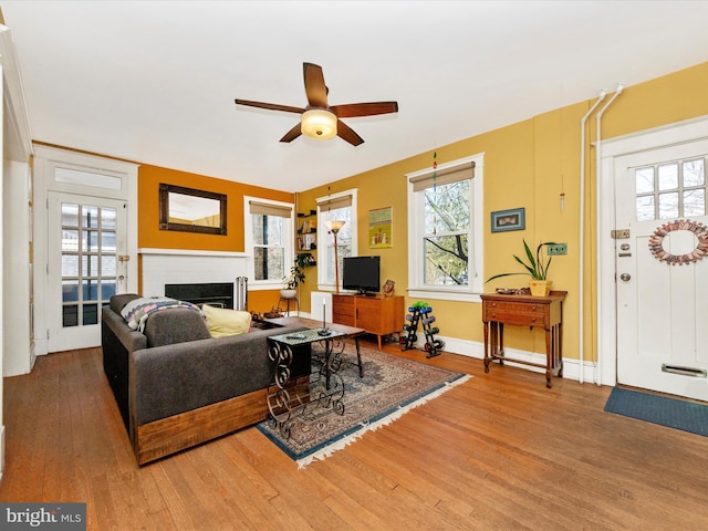 living room with a fireplace, light wood-type flooring, a wealth of natural light, and ceiling fan