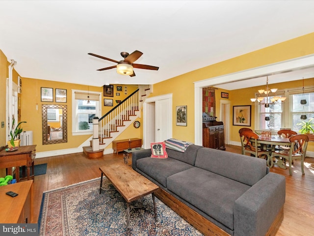 living area featuring stairway, ceiling fan with notable chandelier, baseboards, and wood finished floors