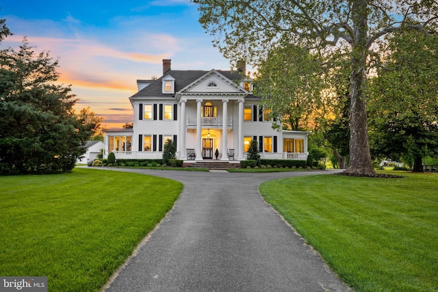 neoclassical / greek revival house featuring a balcony, driveway, a yard, covered porch, and a chimney