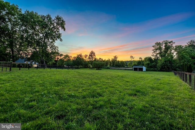 view of yard featuring a rural view, an outdoor structure, fence, and a shed