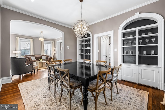 dining space with built in features, dark wood finished floors, arched walkways, crown molding, and a chandelier