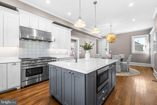 kitchen with under cabinet range hood, ornamental molding, appliances with stainless steel finishes, white cabinetry, and a sink