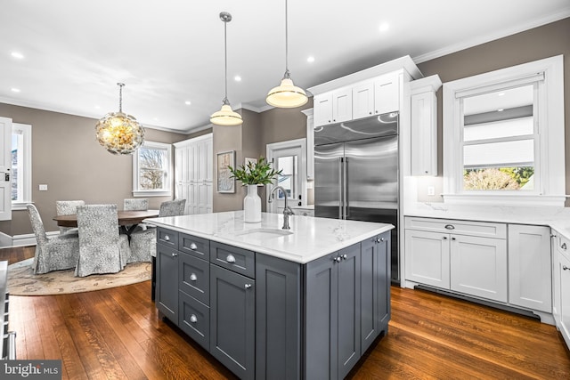 kitchen featuring built in refrigerator, a sink, a kitchen island, white cabinets, and a healthy amount of sunlight