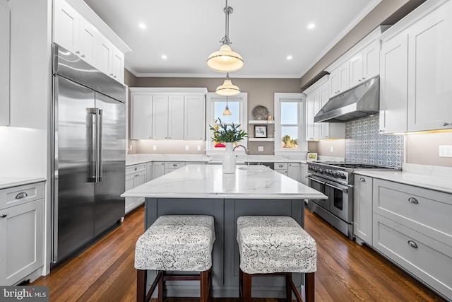 kitchen featuring crown molding, under cabinet range hood, a breakfast bar, dark wood-style floors, and high end appliances