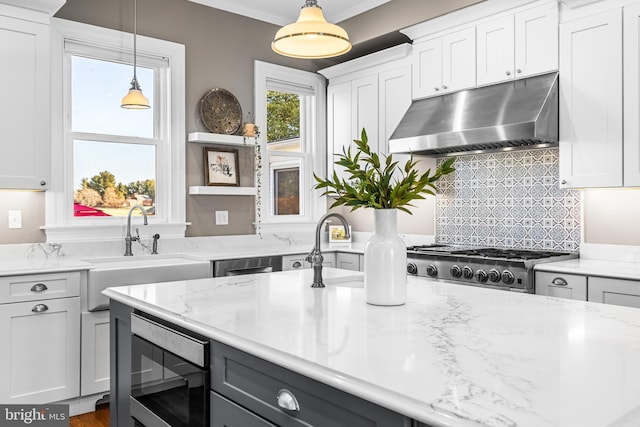 kitchen featuring light stone countertops, a sink, white cabinets, under cabinet range hood, and stainless steel microwave