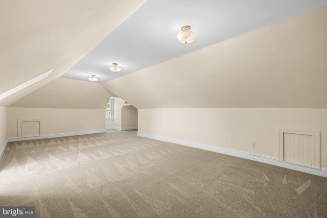 bonus room with light carpet, lofted ceiling with skylight, and baseboards