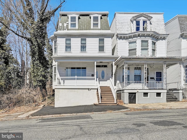 second empire-style home featuring a porch, stairway, and mansard roof