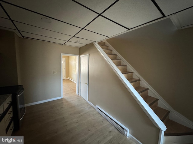 interior space featuring wood finished floors, baseboards, stairs, a paneled ceiling, and baseboard heating