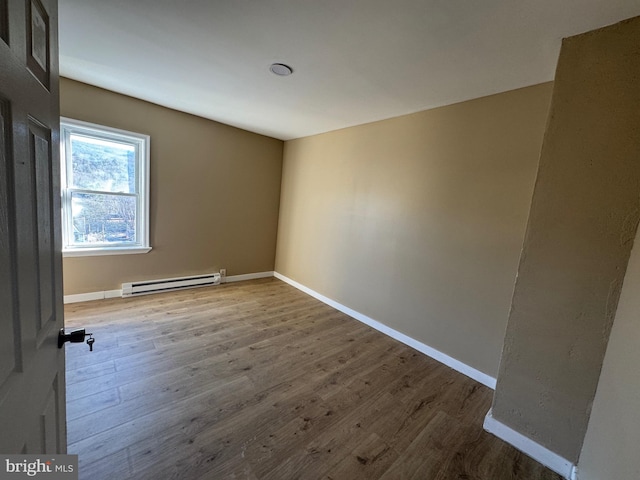 spare room with baseboards, baseboard heating, and wood finished floors