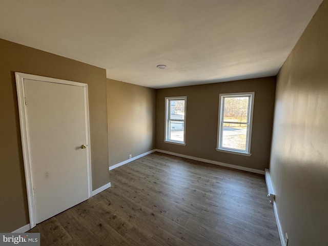 spare room featuring a baseboard radiator, baseboards, and wood finished floors